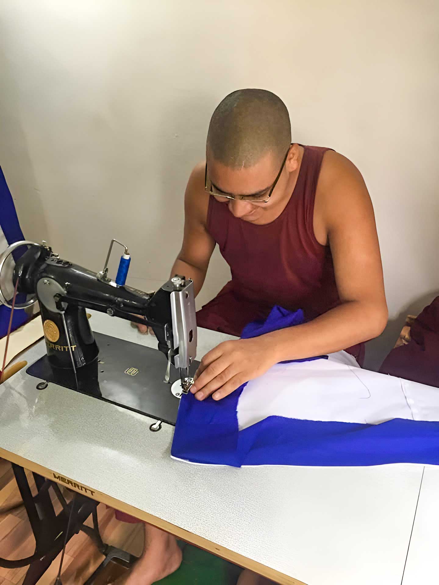 A monk using a sewing machine to work on blue and white fabric.