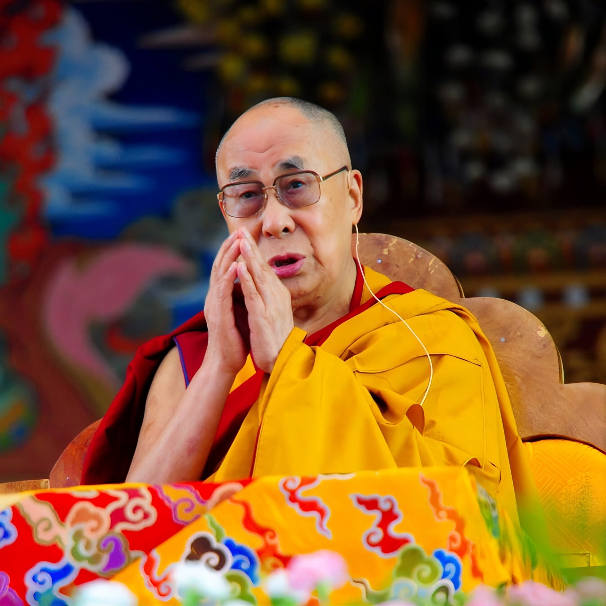 His Holiness the Dalai Lama in yellow and maroon robes with hands together.