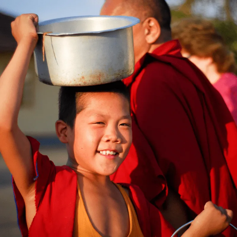 A young monk carrying a large metal pot on their head with a happy expression.