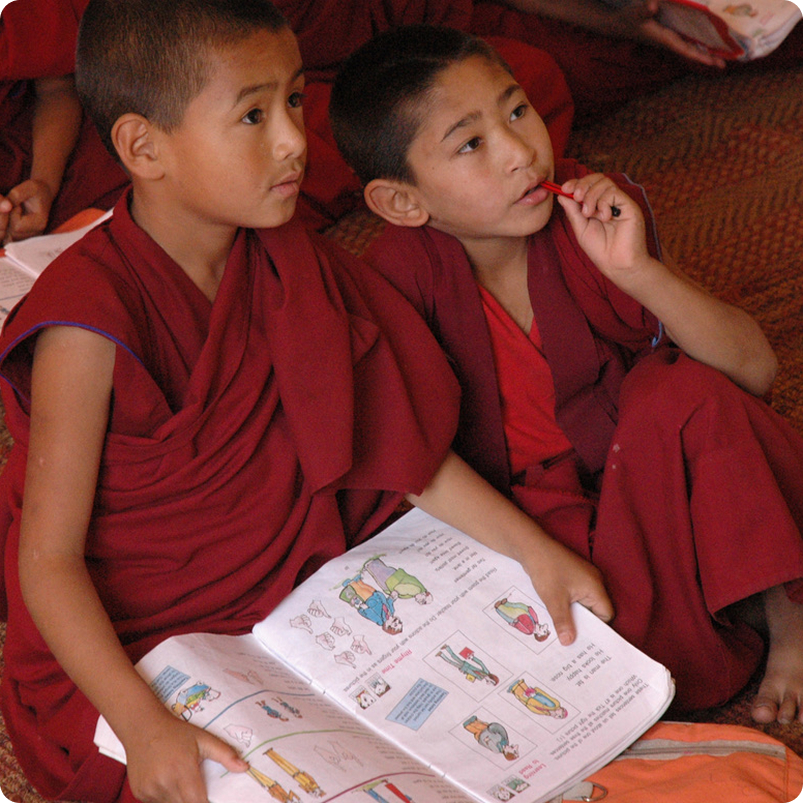 Two children in maroon robes looking at a book together in school.