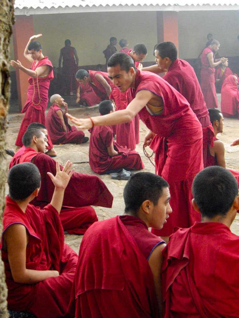 A person in maroon robes gesturing dynamically during a traditional debate.