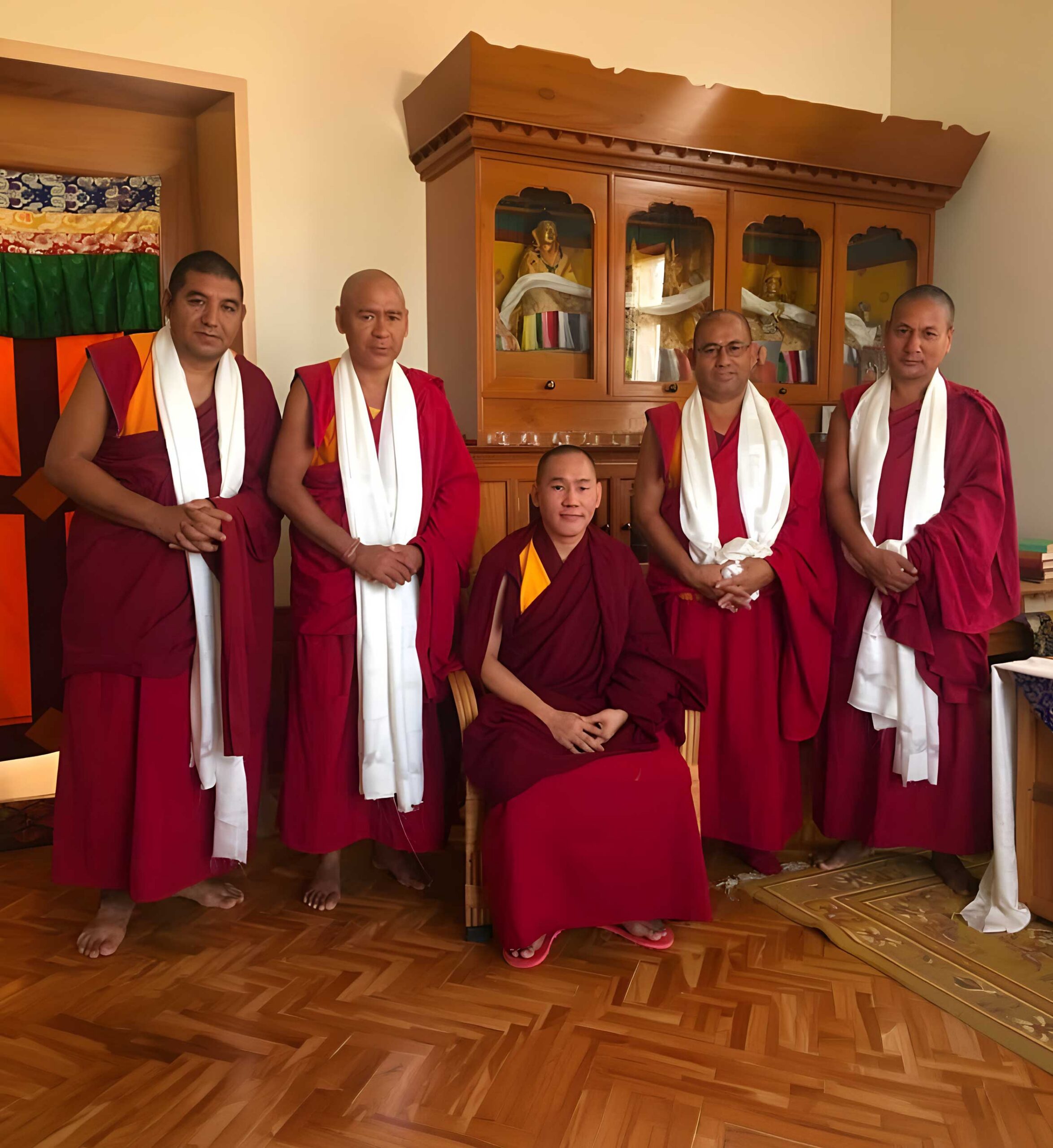 The administrators in maroon and white robes standing together indoors with one seated.