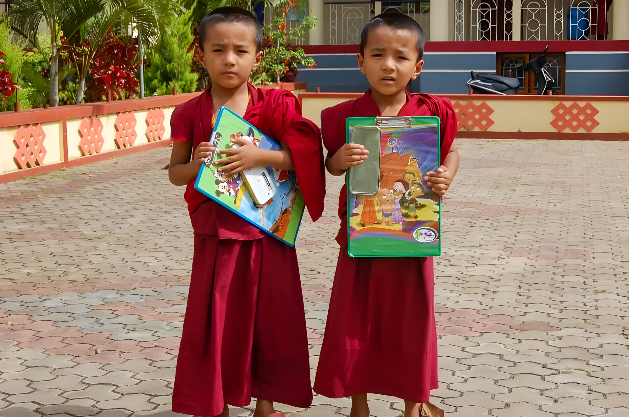 Two children in maroon robes holding up colourful images.