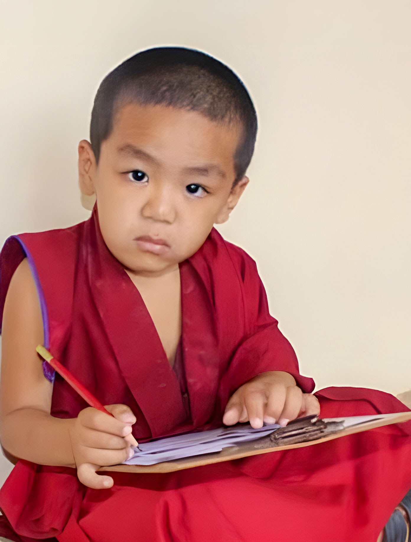 A child in maroon robes writing on a piece of paper.