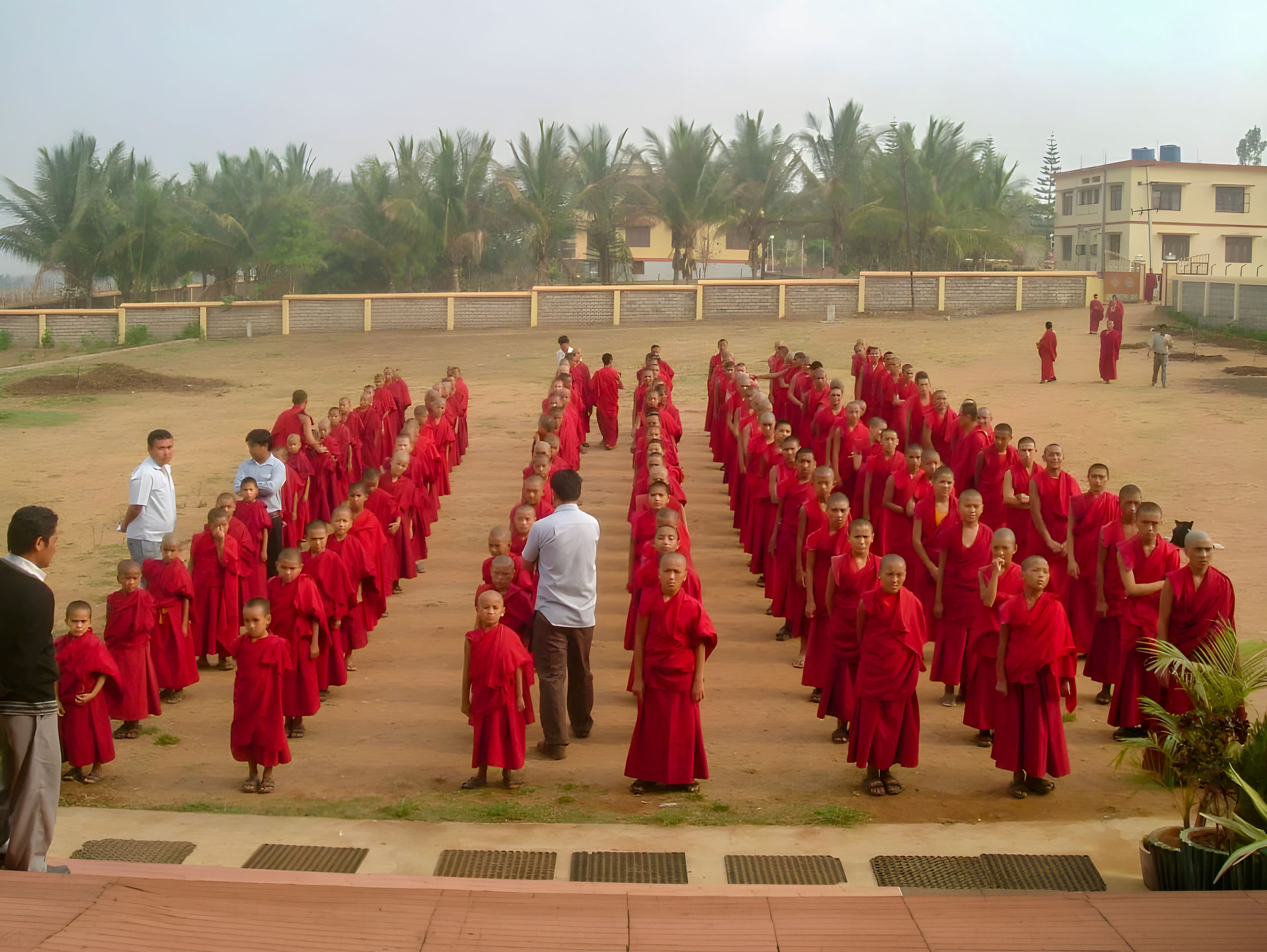 Many school children in maroon robes standing in rows in an outdoor courtyard.