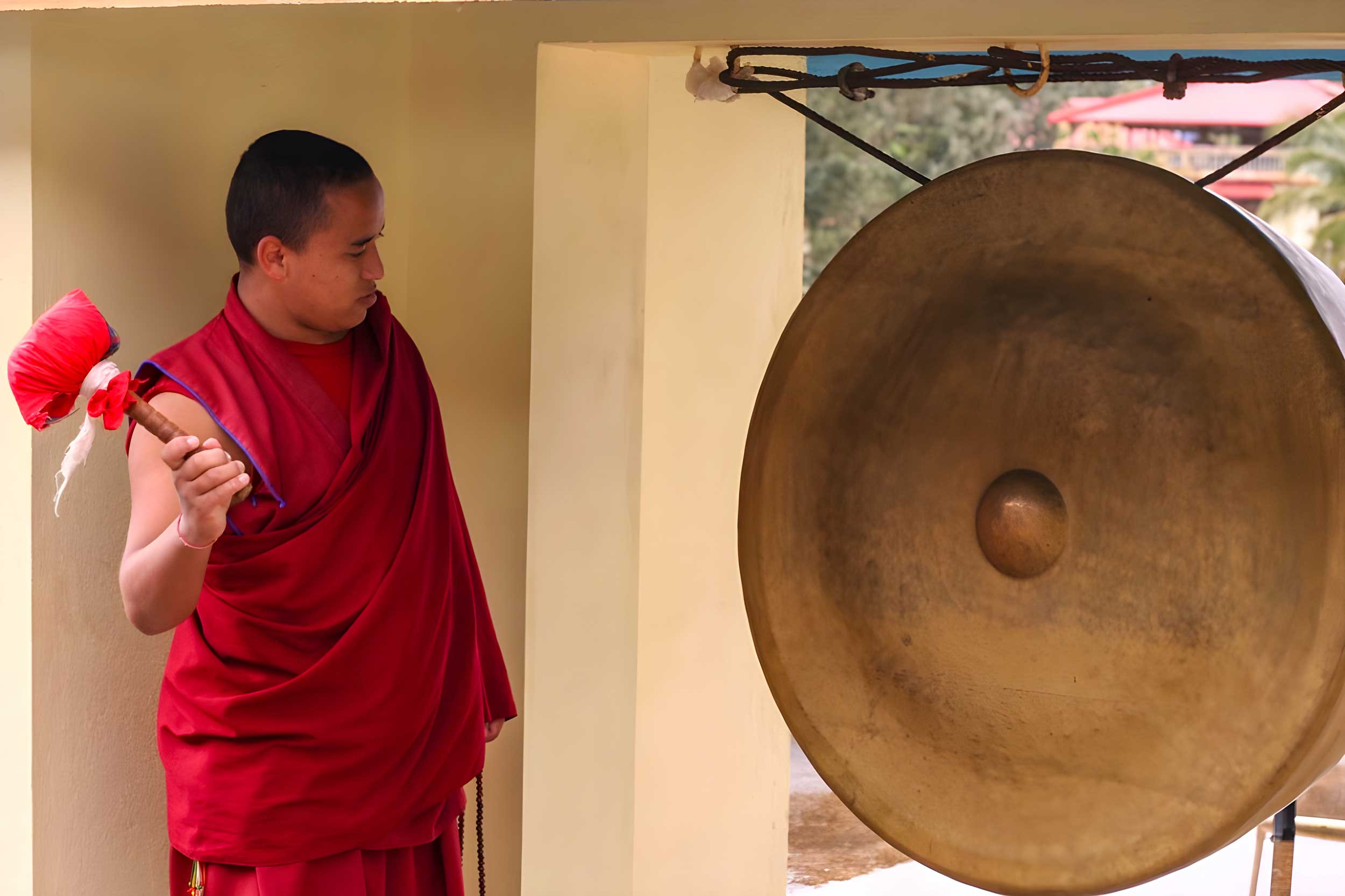 A monk standing next to a large gong ready to hit it.