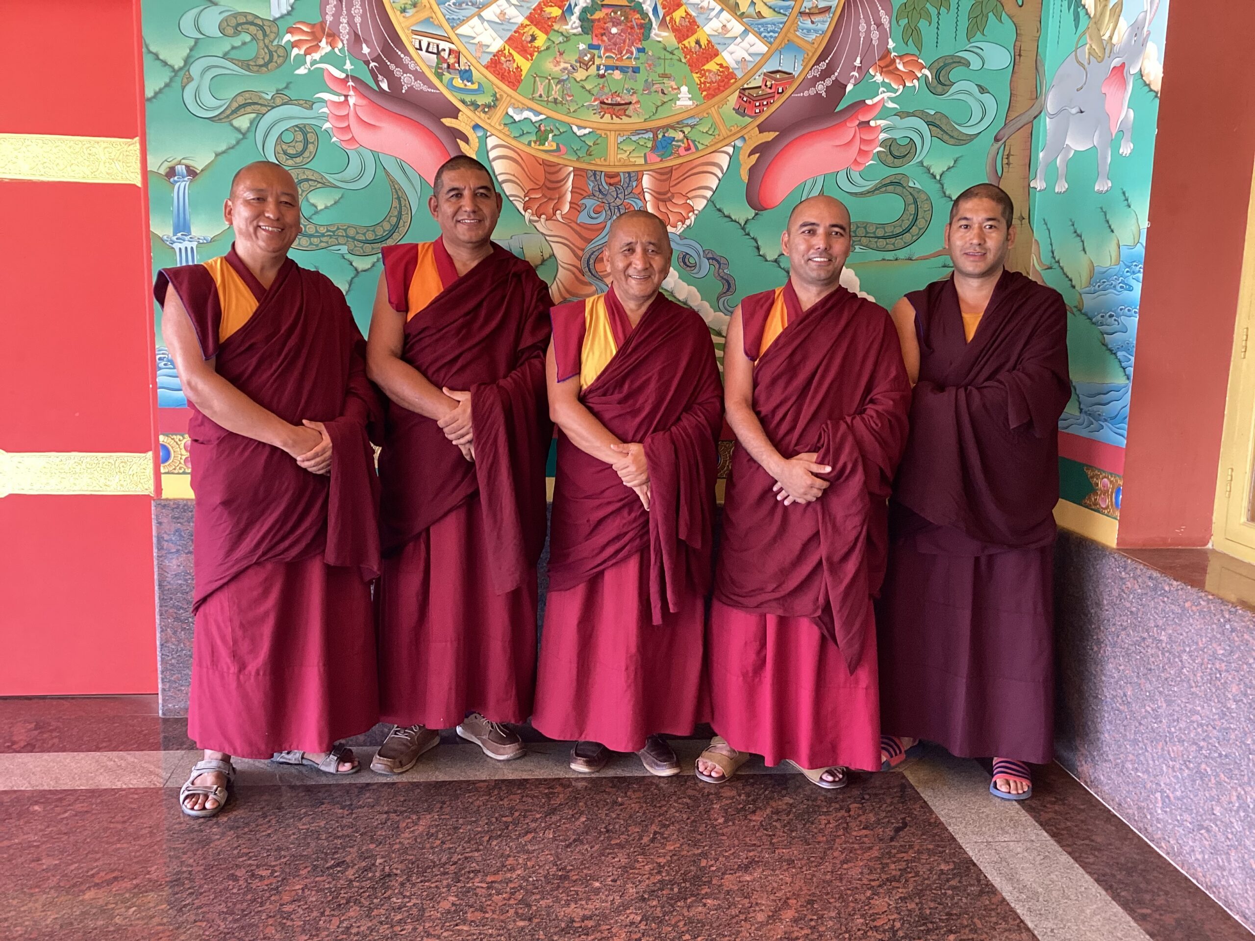 Five monks in maroon robes standing together.