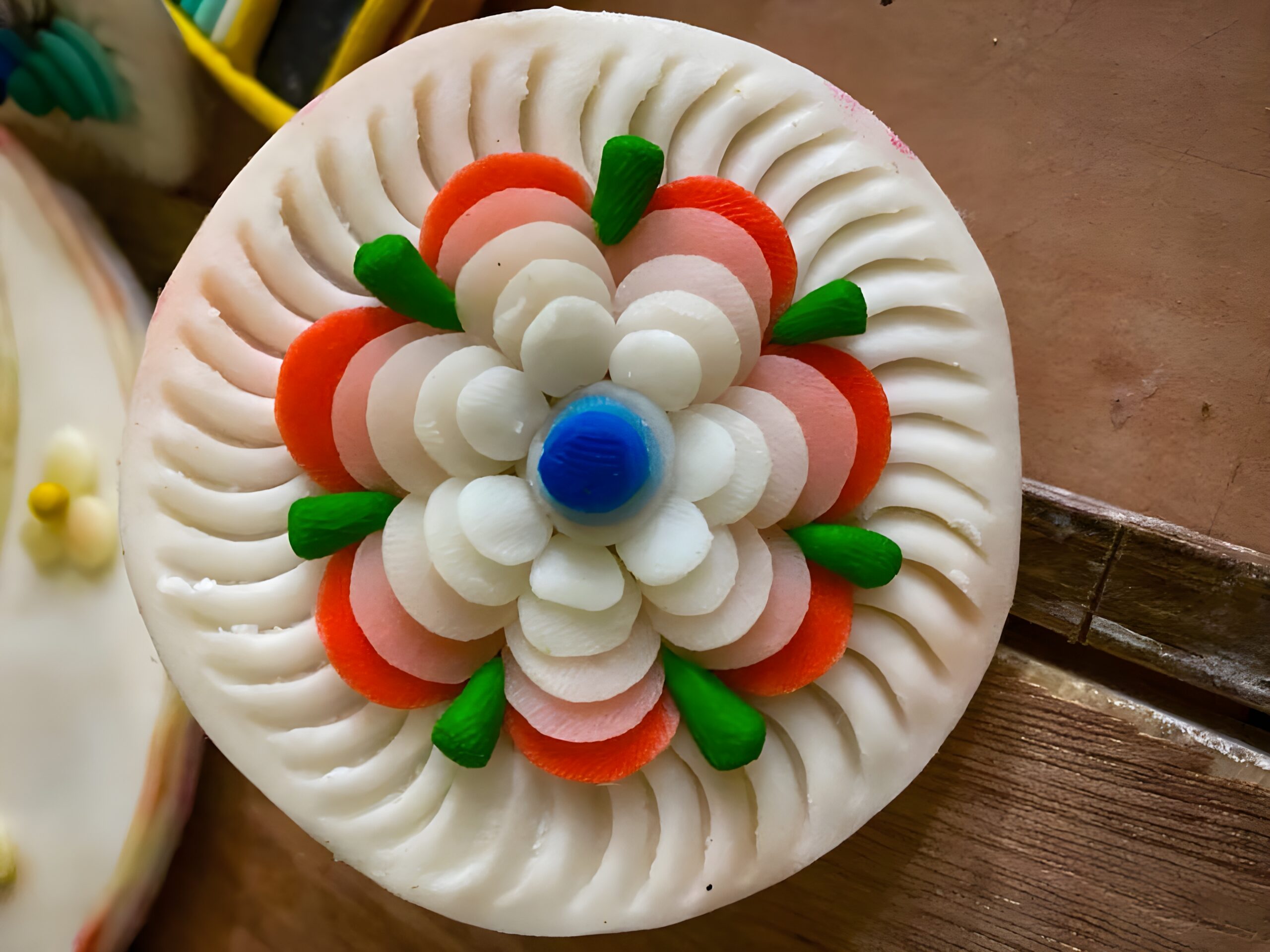 A white, circular ritual butter sculpture decorated with colourful floral patterns.