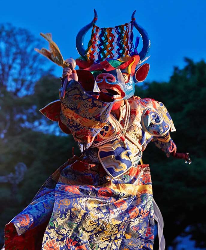 A masked dancer in full costume performing at night.