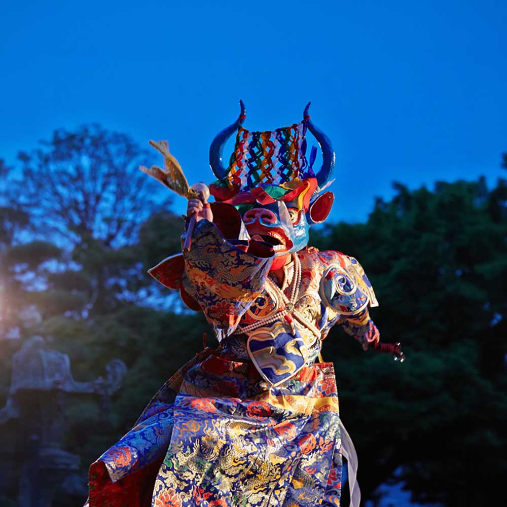 A masked dancer in full costume performing at night.