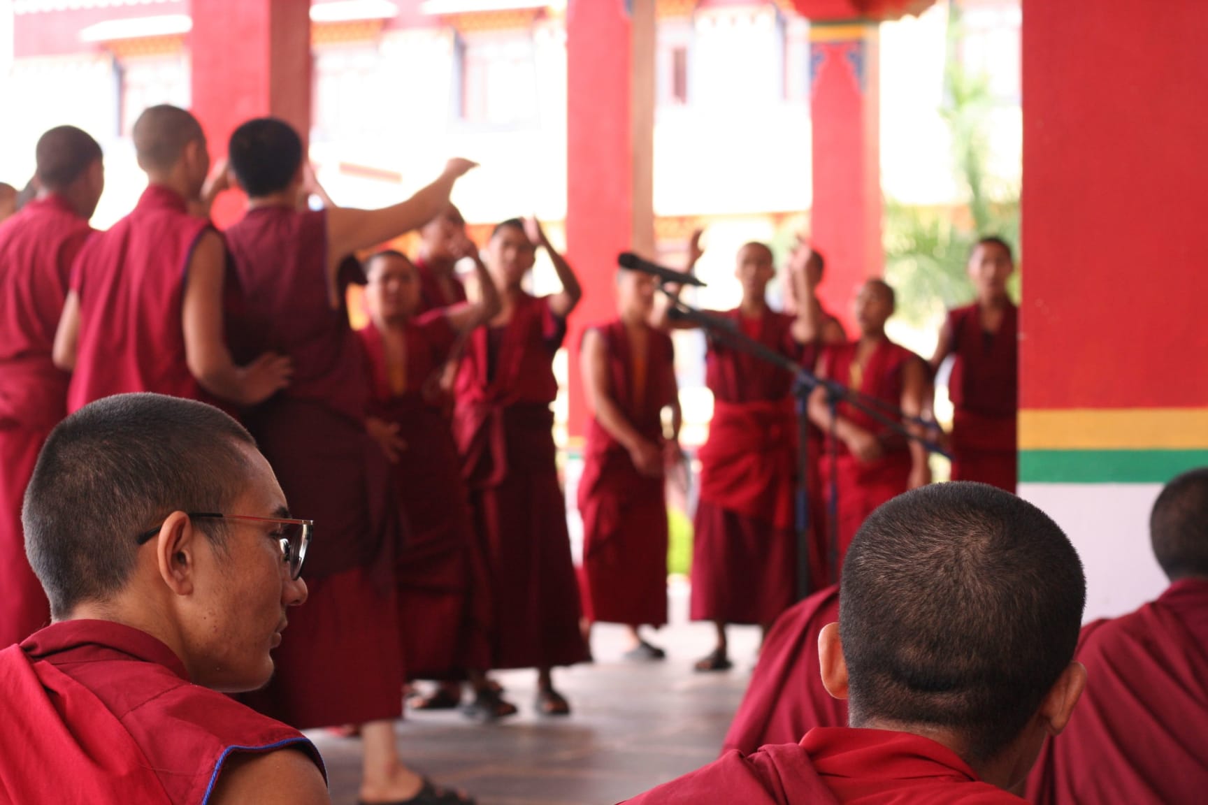 Monks in maroon robes engaging in traditional courtyard debate.