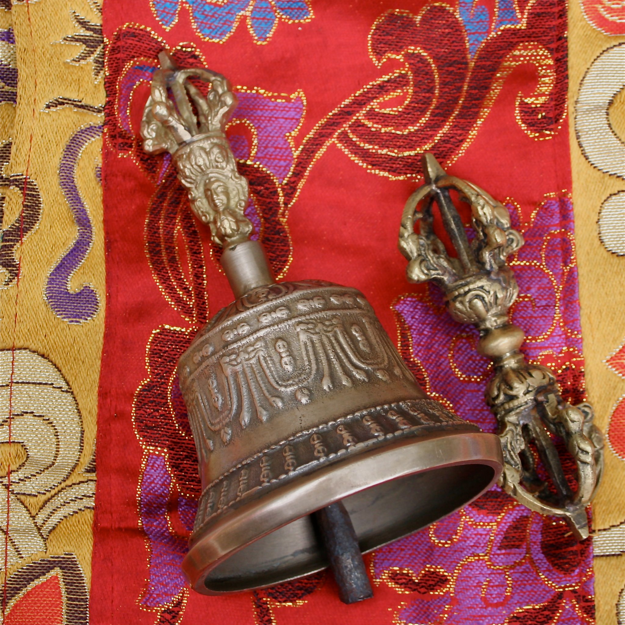 A bronze bell and thunderbolt on red and gold patterned fabric.