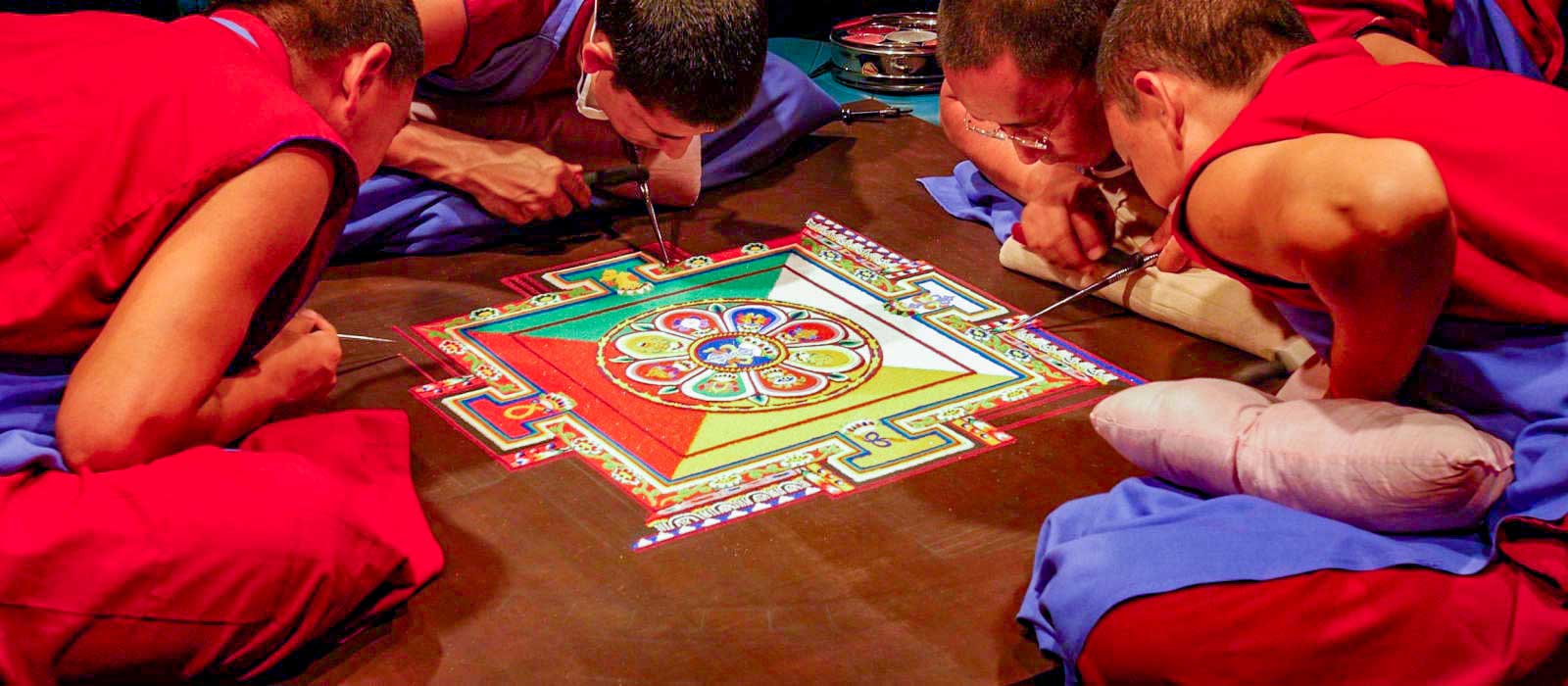 Monks leaning over to apply coloured sand to a mandala.